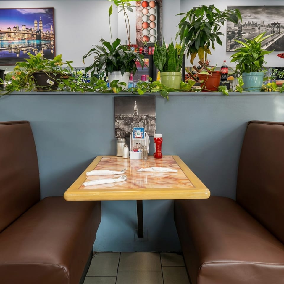 Restaurant booth with a set table, brown leather seating, lush potted plants, and cityscape artwork on blue walls.