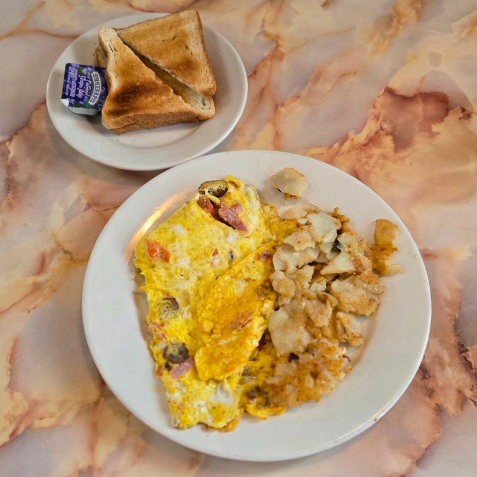 Cheese and mushroom omelet with crispy potatoes, toast, and butter on plates atop a marble diner table.