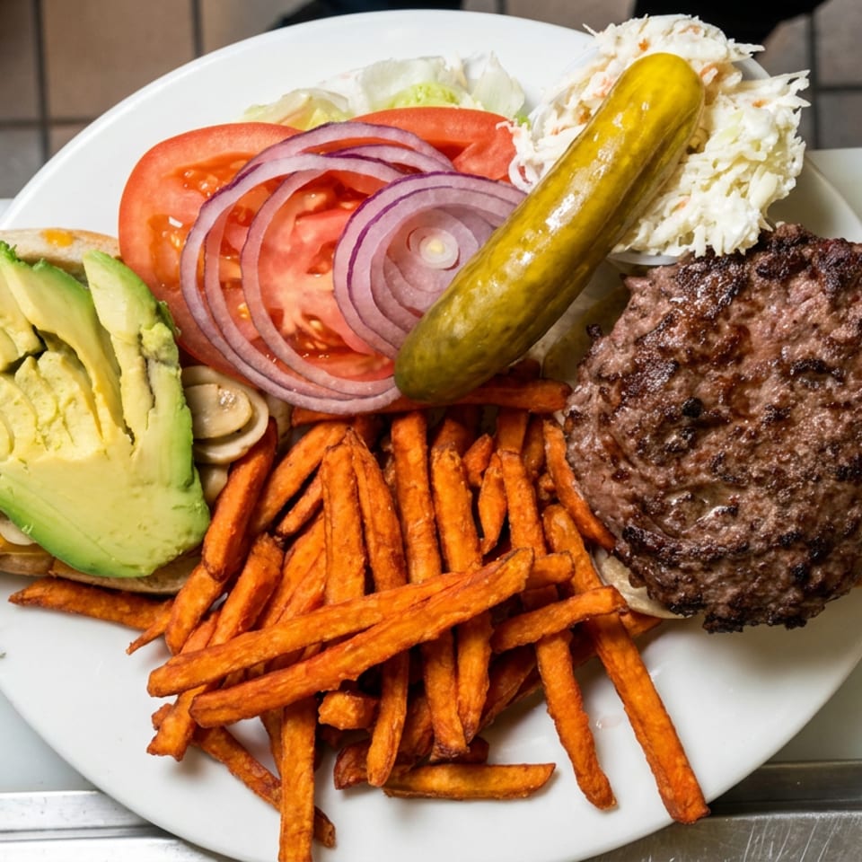 Open-faced grilled beef burger topped with avocado, tomato, red onion, pickle, and coleslaw, served with sweet potato fries.