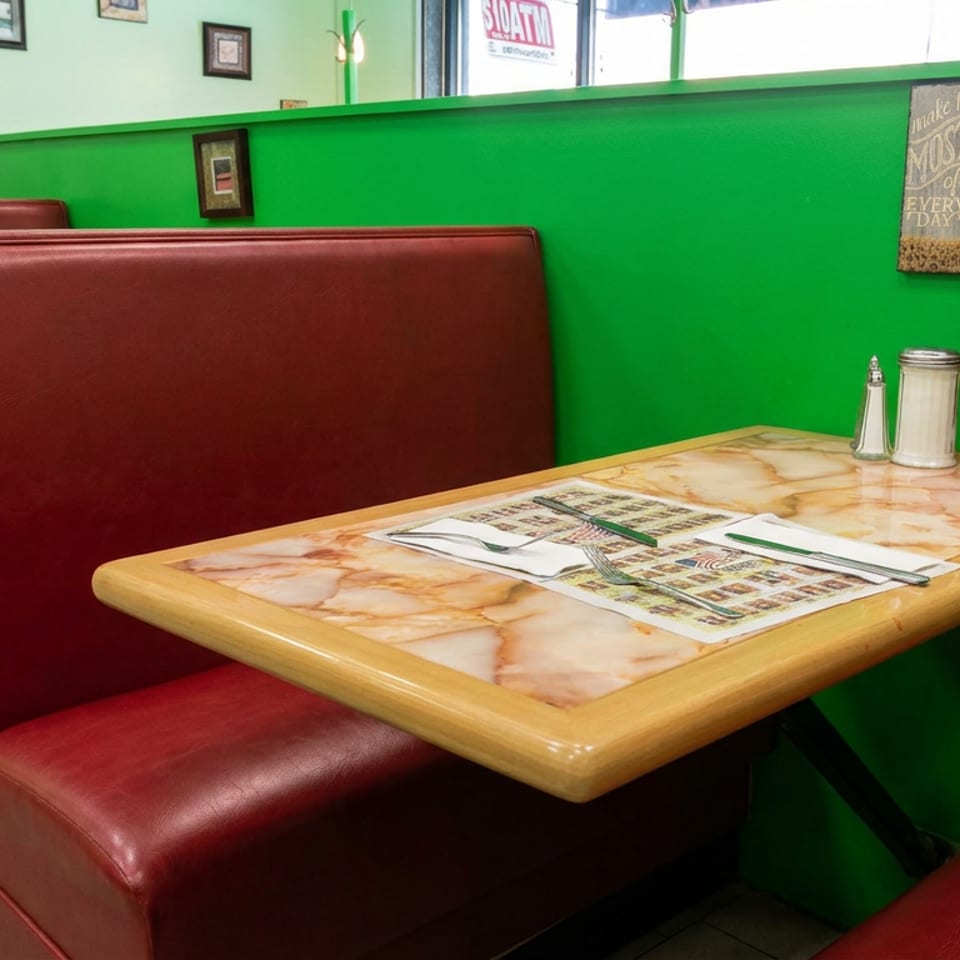 Cozy restaurant booths with burgundy seating, marble-patterned tables, menus, condiments, and bright green walls.